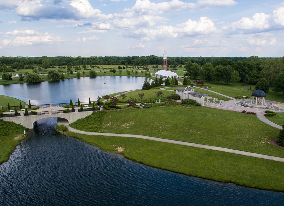 Carmel, IN - Aerial View of Park With a Small Concrete Bridge Crossing a Lake