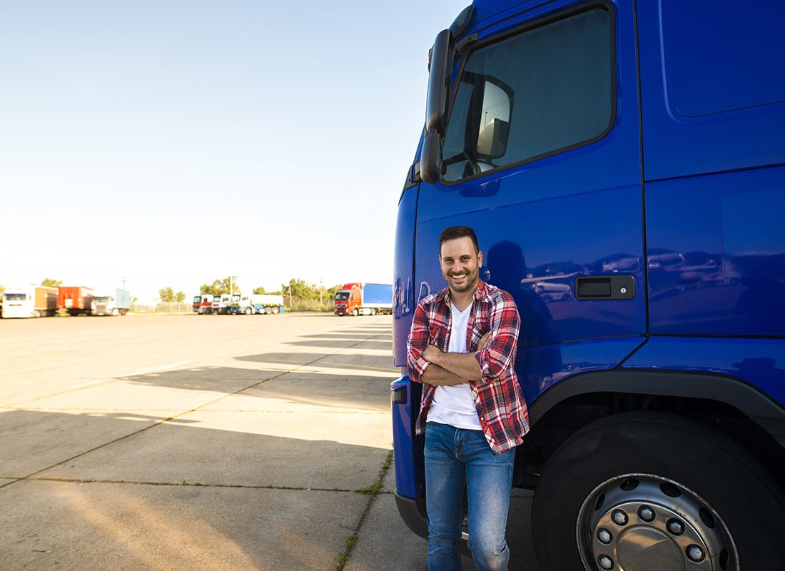 Insurance by Industry - Smiling Truck Driver Leans on His Blue Truck During a Sunny Day at a Parking Lot